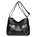 Borsa a tracolla in pelle nera con ricamo floreale e tracolla regolabile su sfondo bianco - Nero