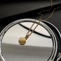 Collana minimalista dorata con ciondolo rotondo Good Luck riflessa in uno specchio - Oro