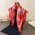 Elegante foulard in seta con stampa geometrica rossa e arancione appeso a una gruccia - Rosso