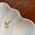 Gold necklace with square shell smiley face pendant on a white decorative plate - Gold