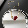 Elegante goldene Schlangenkette mit zwei tiefroten Perlen auf einer Spiegelfläche - Rote Perlenkette (05-G17)