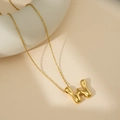 Collier doré avec pendentif lettre H style lave fluide sur fond beige texturé - Lettre Bulle W (Avec Chaîne Cruciforme)