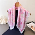 Pink paisley print faux silk square scarf displayed on a black dress and wood hanger - Pink