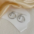 Macro detail of silver spiral drop earrings with metallic curves on white stone and silk - Silver Color (E101)