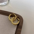 Orecchini a cerchio dorati con texture ondulata presentati su un vassoio in legno - Oro