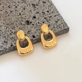Macro detail of U-shaped gold earrings with vertical ribbed texture on stone surface - Gold