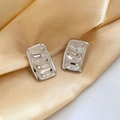 Nahaufnahme silberner rechteckiger Ohrstecker mit Hammerschlag-Textur auf Champagner-Satin - Silber (G305)