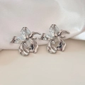 Macro shot of silver-toned iris flower earrings with metallic texture on white silk - Silver