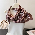 Detail of leopard print silk scarf tied on white knit top showing smooth satin texture - Brown