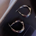 Dettaglio ravvicinato di orecchini a cerchio in metallo argentato intrecciato ed elegante - Argento
