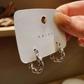 Primer plano de pendientes de aro plateados con diseño trenzado en tarjeta blanca - Plateado