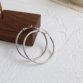 Detailed view of large polished silver hoop earrings placed on a premium dark wood base - Silver (4cm)