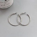 Close-up of polished silver hoop earrings on a minimalist grey surface with a candle - Silver (5cm)