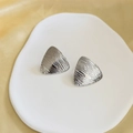 Dettaglio di orecchini triangolari argentati con superficie metallica testurizzata in stile minimal - Argento (G209)