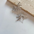 Detailed macro view of silver sunburst spike earrings on beige stone texture - Silver (D218)