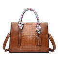 Close-up of brown crocodile embossed tote bag with decorative silk scarf on handle - Brown