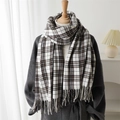 Plaid cashmere-like winter scarf with tassels worn over a grey coat in cozy setting - Black Brown
