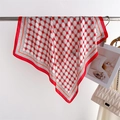 Detail of red geometric silk scarf draped on a metal bar with a white quilted handbag - Red