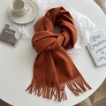 Detail of caramel knit scarf featuring elegant long fringes and a leather brand label - Orange