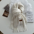 Close-up of fluffy cream knit scarf featuring long fringe edges and leather logo patch - Cream