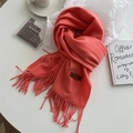Close-up of coral pink knit scarf featuring long tassels and a brown leather brand tag - Kumquat Yellow