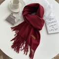 Detail of burgundy thick wool scarf with fringes and leather label on white table - Burgundy