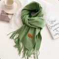 Close-up of grass green knit scarf featuring soft fringe and a leather logo label - Avocado Green