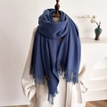 Close-up of blue tassel scarf with a brown leather label on a beige coat detail - Denim Blue