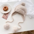 Beige knitted balaclava with soft fur pom-poms and brand label on a minimal desk - Beige