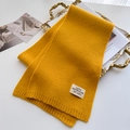 Detail eines ingwergelben Strickschals mit feiner Textur und modischem Markenetikett - Ingwergelb