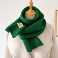 Detail eines smaragdgrünen Strickschals mit weißem Webetikett auf beigem Mantel - Smaragdgrün