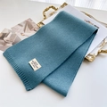 Détail d'une écharpe en maille bleu-gris avec texture côtelée et étiquette de marque - Bleu lac