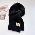 Détail d'une écharpe en maille noire avec une étiquette tissée blanche et texte sur fond épuré - Noir