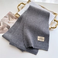 Détail d'une écharpe longue en maille grise avec étiquette minimaliste sur bureau blanc - Gris clair