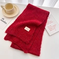 Detail of bright red chunky knit scarf with fabric tag on a cozy lifestyle desk setup - Red