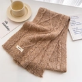 Detail shot of chunky cable knit wool scarf texture in camel with a branded woven label - Khaki