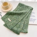 Detailed macro view of green cable knit wool scarf texture with brand label and fiber flecks - Green