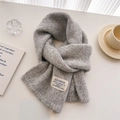 Detailed texture of a soft light grey wool knit scarf with a stylish woven label on a table - 156x24cm / Gray