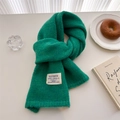 Close-up of green wool knit scarf with brand label on a cozy decorated table - 156x24cm / Green