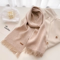 Detail of pink-beige knit scarf with fine tassels and a brown handmade leather tag - Oatmeal