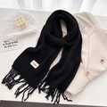 Close-up of black cable knit wool scarf with tassels and white label detail on a jacket - Black