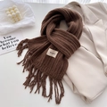 Detail of dark brown knitted wool scarf with tassel fringe and white brand label - Coffee