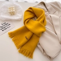 Detail of yellow knit scarf featuring fringed edges and handmade leather tag on suit - Yellow