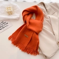 Close-up of orange knit scarf with tassel fringe and a brown leather Hand Made label - Orange
