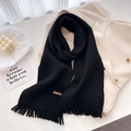Close-up of black knitted scarf with fringe and a brown leather handmade label - Black