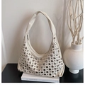 Detalle del bolso hobo crema con remaches metálicos plateados sobre libros, fondo minimalista - Blanco