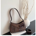 Brown vintage underarm bag with metal eyelets and zippers resting on a white book - Brown