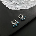 Silberne Creolen mit drei blauen Evil-Eye-Anhängern auf dunkler Texturfläche - Silber