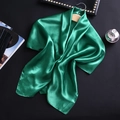 Texture détaillée du foulard en satin de soie vert émeraude drapé sur un cintre en bois - Vert fruit