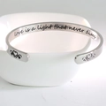 Vista ravvicinata del bracciale rigido in acciaio inox con citazione incisa - L'amore è una luce che non si spegne mai